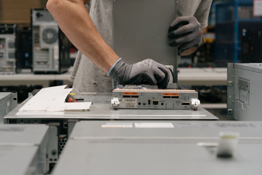 Aufbereitung von IT-Hardware: Ein Laptop wird von einem Menschen repariert, der graue Handschuhe trägt.