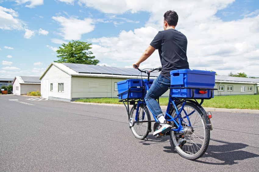 Lastenräder sind für die interne Mobilität in der Industrie gut geeignet, da oft lange Wege auf dem Betriebsgelände zurück gelegt werden. Das Bild zeigt einen Fahrradfahrer mit Transportrad auf einer Straße